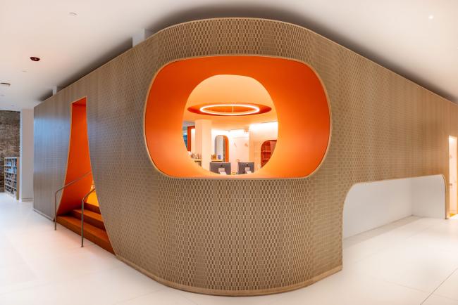 A corner shot of the Adams Street Library children's section looking from the main entrance. The wall is curved and textured wood and the opening window into the children's section is orange.